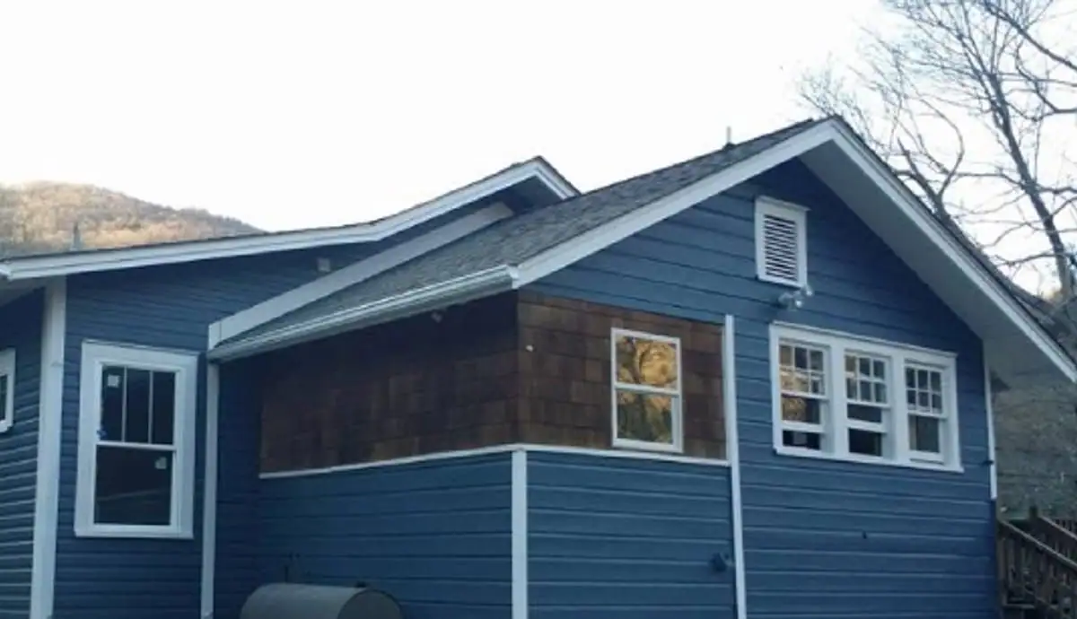 Blue lap siding and white trim on a house below a wooded mountain ridge