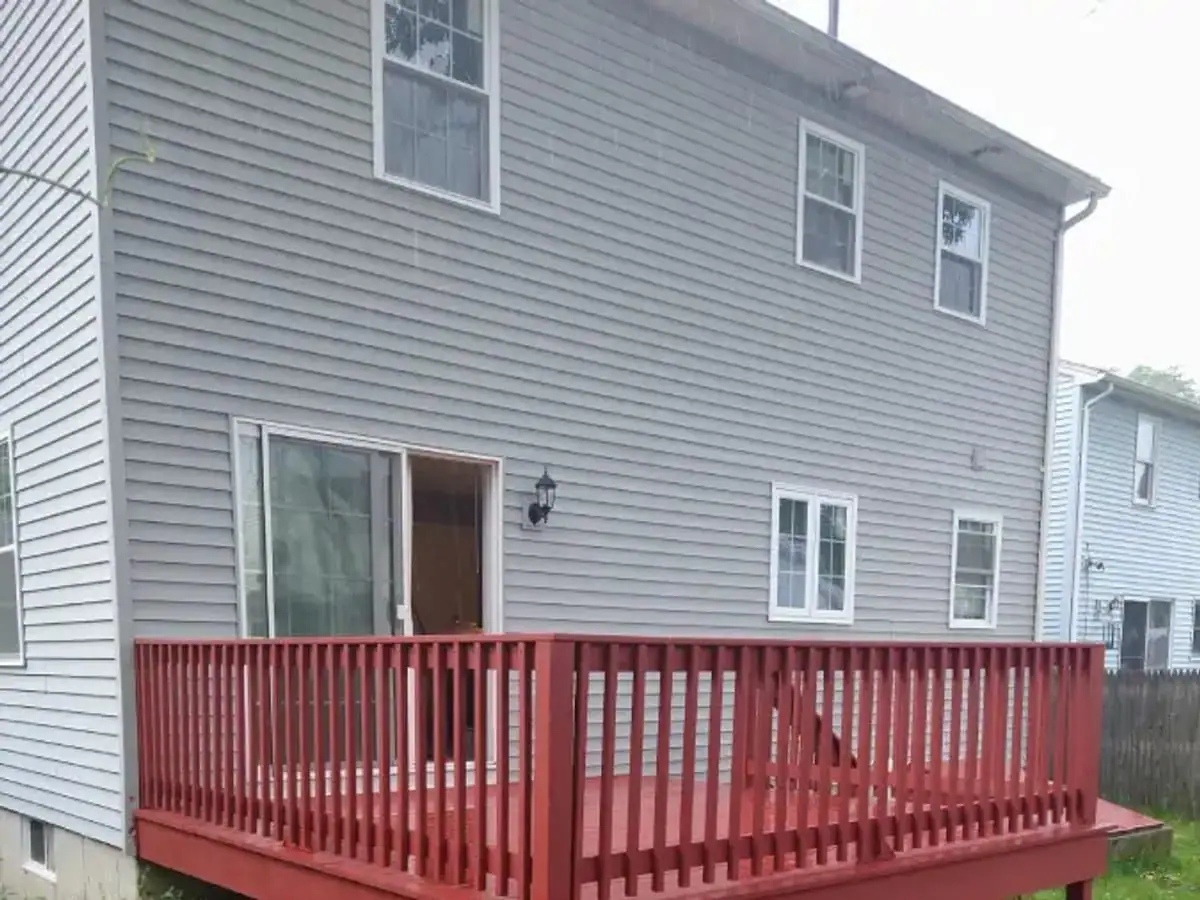Deck and railing finished in solid red behind a two story house with gray siding